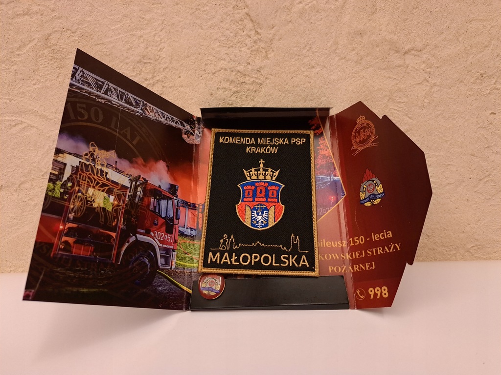 Jubileuszowa broszura z rzepem z logo Krakowa i przypinką Straży Pożarnej