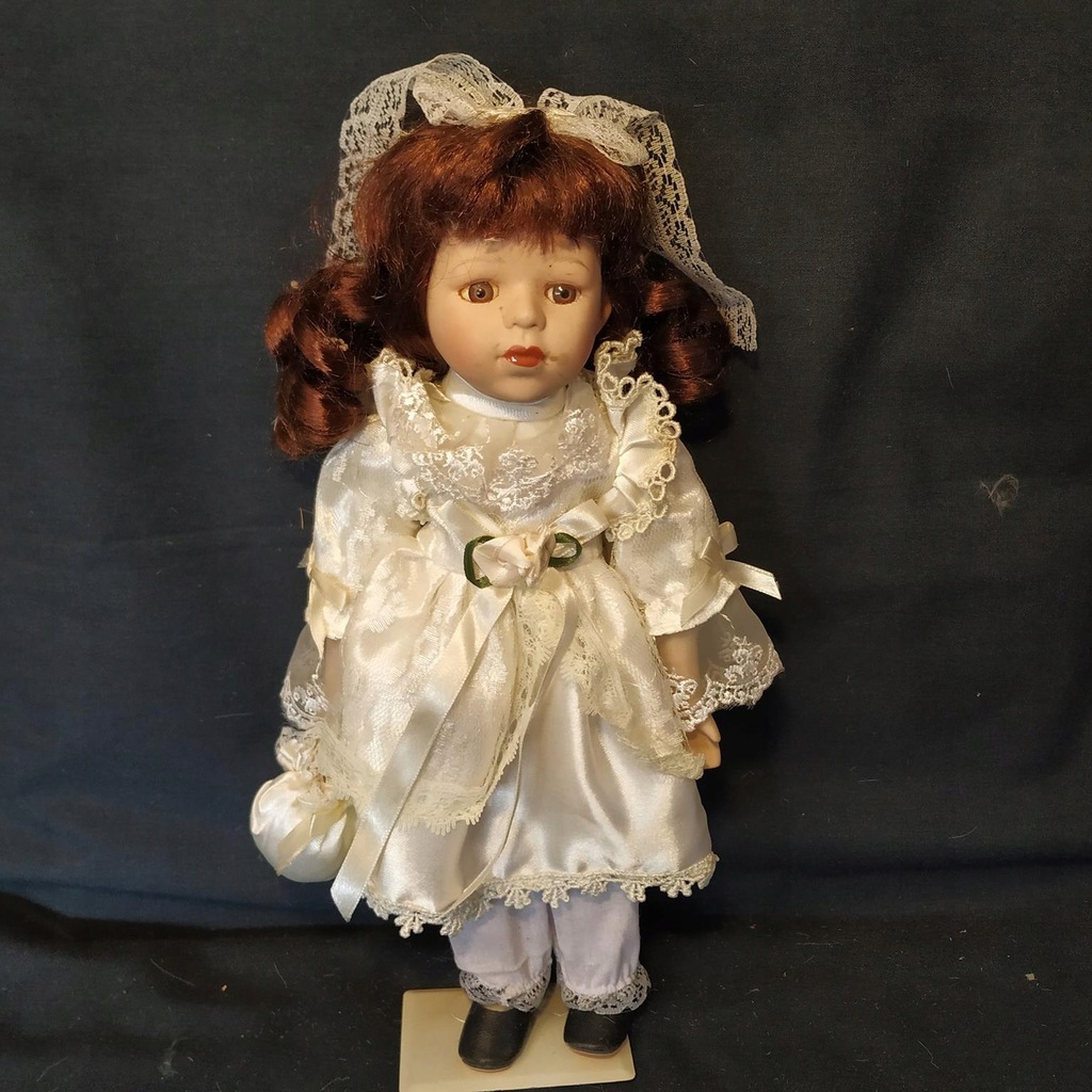Kolekcjonerska lalka porcelanowa na stojaku.