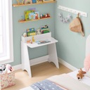 Белый письменный стол для ребенка с полкой для книг, низкими художественными принадлежностями.