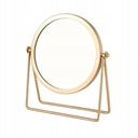 Золотое круглое косметическое зеркало, стоящее на женском туалетном столике.