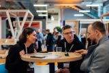Conference table, orange, wood, three people seated, drinks, name tag.