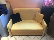 Żółta rozkładana kanapa z dwiema poduszkami 