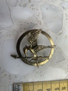 Metalowa przypinka nawiązująca do książki i filmu Igrzyska śmierci