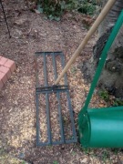 Ręczny niwelator terenu z drewnianym trzonkiem.