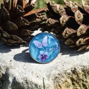 pierścień z żywicy z motylem i kwiatami na niebieskim tle