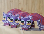 Trzy fioletowo-czerwone drewniane figurki kotów z Bali 