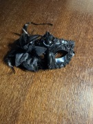 czarna maska karnawałowa w stylu weneckim ozdobiona jest kwiatem i cekinami