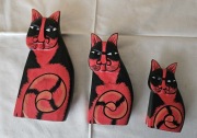 Trzy czerwono-czarne drewniane figurki kotów z Bali 