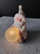 Świąteczna figurka Świętego Mikołaja trzymającego świecącą kulę.