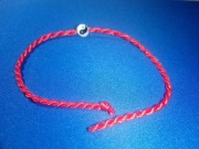 Czerwona nić z zawieszką, ochrona przed złymi mocami.