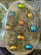 Drewniane jajko ozdobione naturalnym siankiem i jajkami z czekolady 