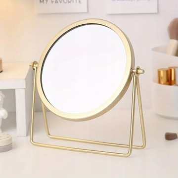 Золотое круглое косметическое зеркало, стоящее на женском туалетном столике.