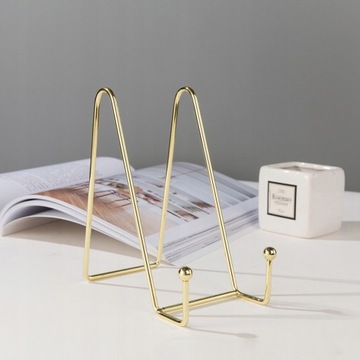 На столе стоит книга, металлический мольберт.