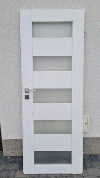 Białe drzwi z mlecznymi szybami i srebrną klamką 